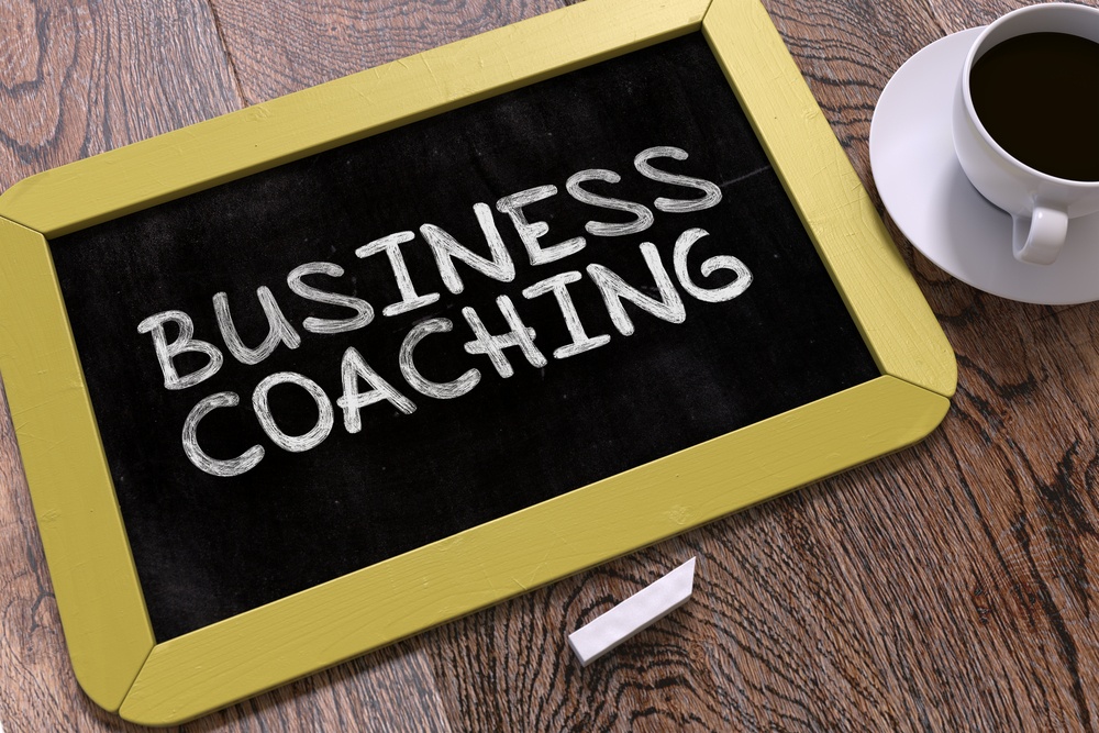 Handwritten Business Coaching on a Yellow Chalkboard. Top View Composition with Chalkboard and White Cup of Coffee. 3D Render..jpeg